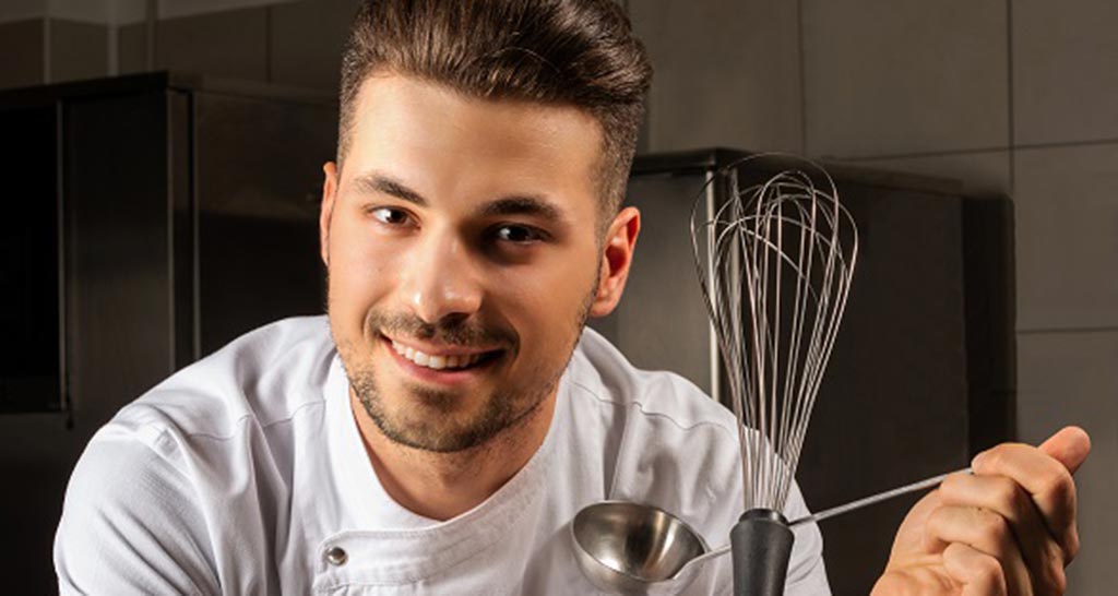 Chef sorridente con frusta e mestolo. Cucina professionale.
