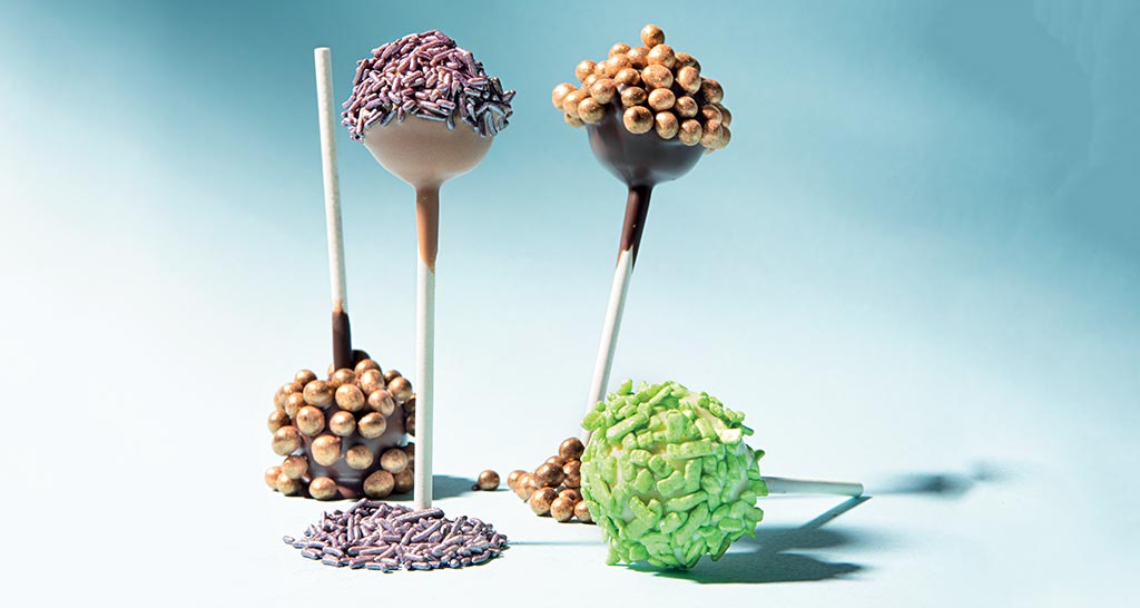 Cake pops assortiti su sfondo azzurro. Dolcetti decorati con palline e zuccherini colorati. Pasticceria creativa.