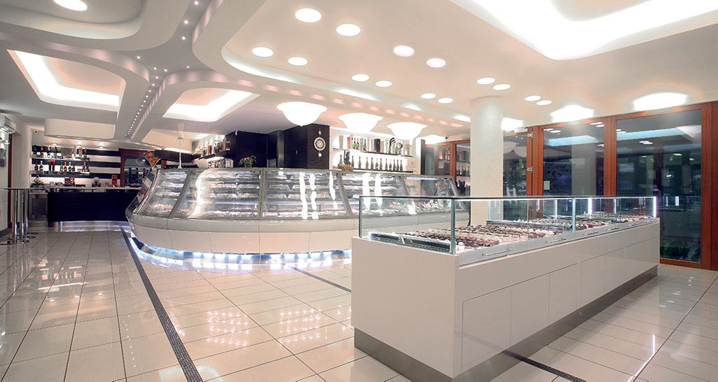 Interno di pasticceria: vetrine di dolci, illuminazione moderna, design elegante.