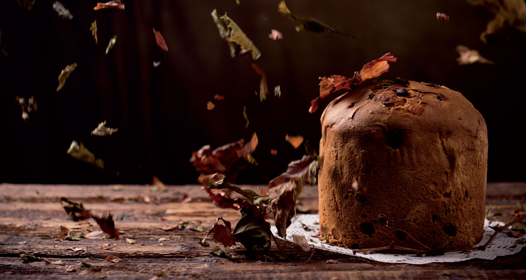 Panettone artigianale su legno con foglie autunnali. Dolce lievitato tradizionale.