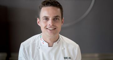 Ritratto di Etienne Leroy, chef pasticcere sorridente in uniforme bianca.