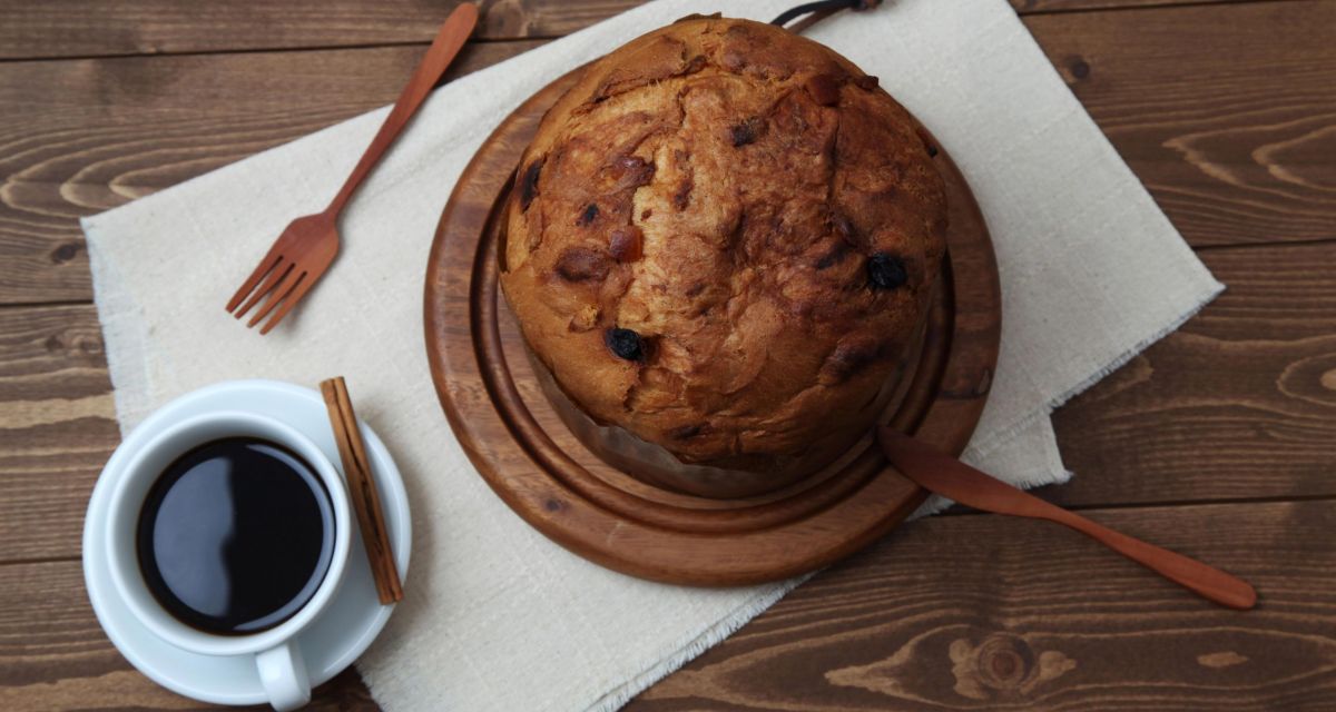 Panettone artigianale su tagliere con caffè e cannella. Dolce natalizio italiano.