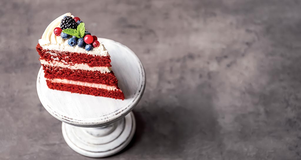 Fetta di torta red velvet con frutti di bosco freschi su alzata bianca. Dessert goloso.