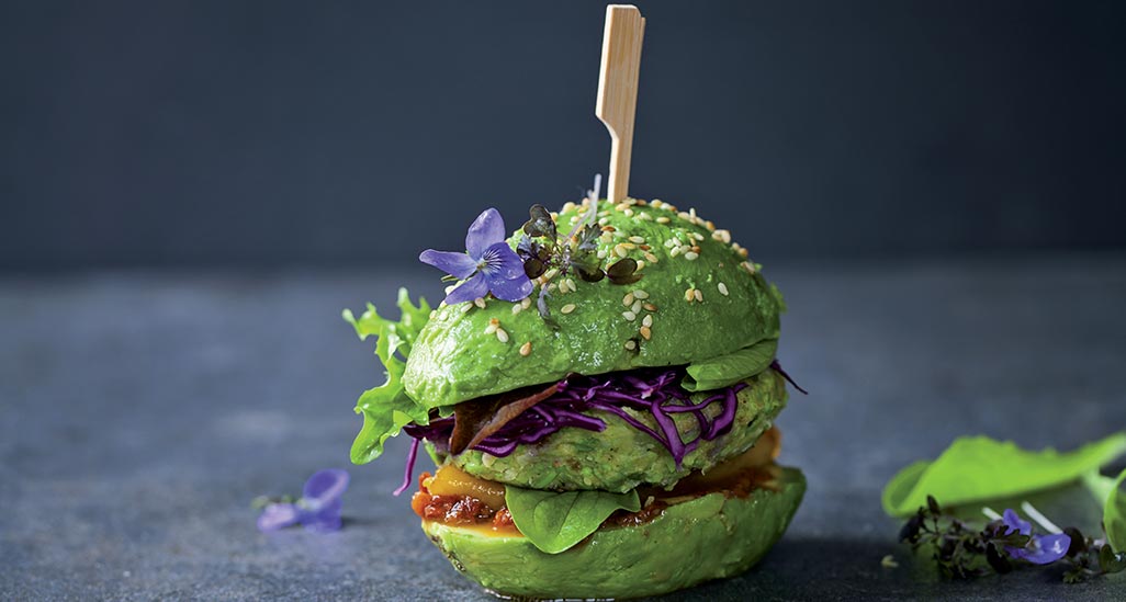 Hamburger vegano colorato con avocado, semi di sesamo e fiori eduli. Cibo sano e originale.