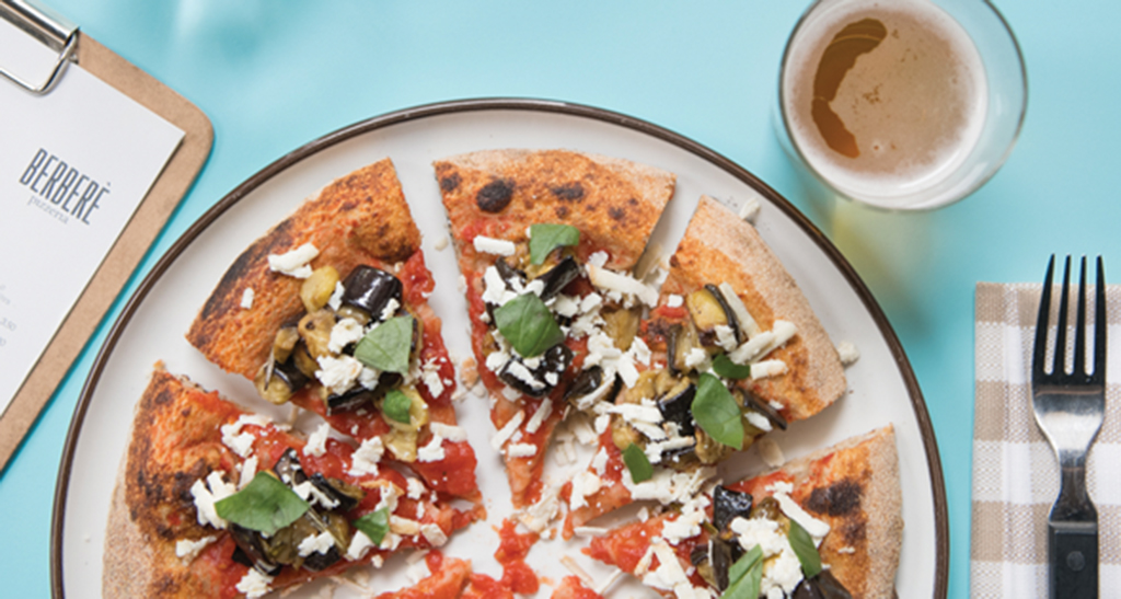 Pizza artigianale con melanzane, pomodoro e basilico. Birra chiara.