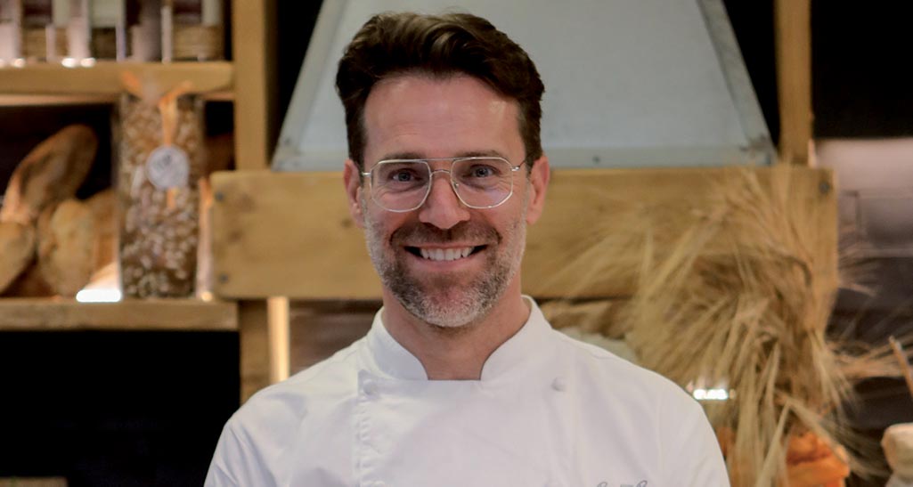 Ritratto di Renato Bosco, chef e pizzaiolo italiano, con divisa da cuoco e occhiali. Sorride.