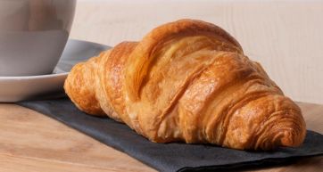 Croissant dorato su tovagliolo nero. Colazione con croissant e caffè.