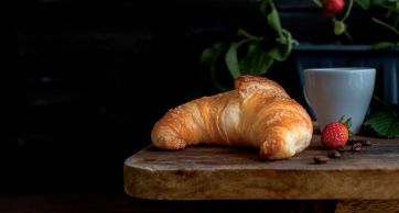 Croissant dorato con caffè e fragola su tagliere di legno. Colazione italiana.