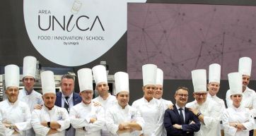 Team di pasticceri con Mario Solinas all'Area Unica Unigrà. Chef in divisa bianca e cappello.