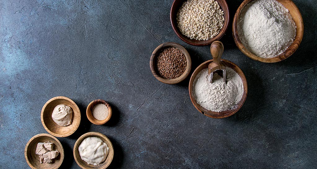 Farine e mix in ciotole di legno: farina integrale, lievito, semi di lino. Ingredienti per pane e pizza.