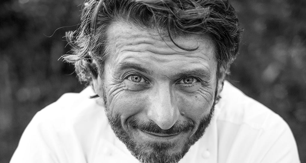 Ritratto in bianco e nero dello chef Massimiliano Scotti, sguardo intenso e sorriso accennato.