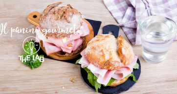 Due panini gourmet con mortadella su taglieri, tovagliolo a quadri e bicchiere d'acqua. Delizioso cibo italiano.