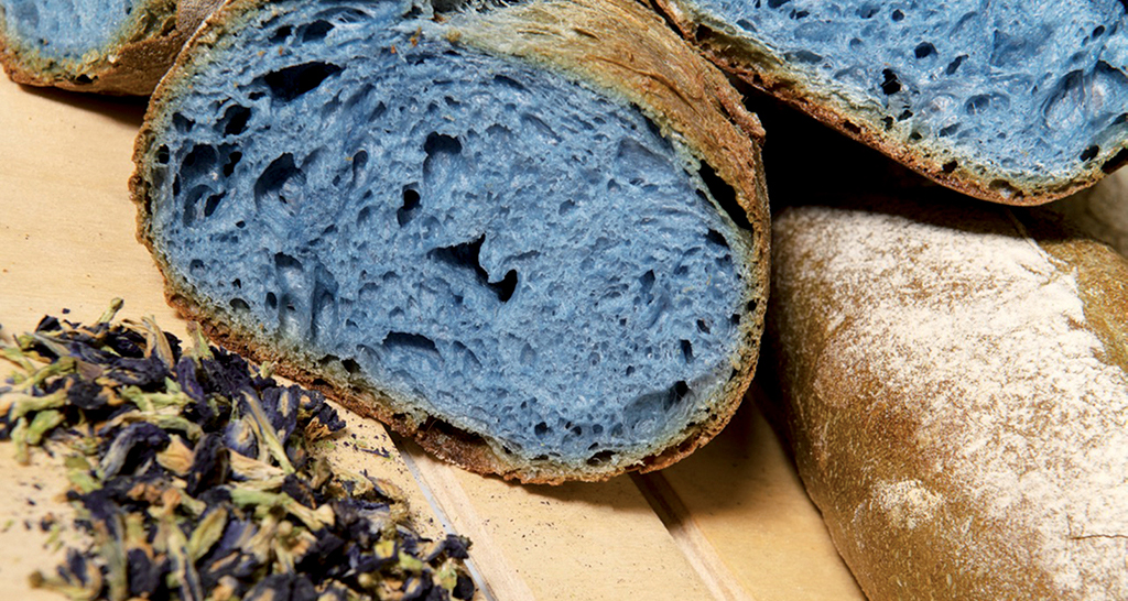 Pane blu artigianale. Fetta di pane azzurro con fiori eduli. Cucina creativa, ricetta insolita.
