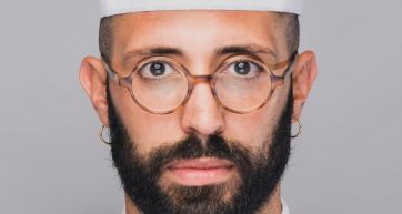 Ritratto di Sebastiano Caridi, chef con occhiali tondi e barba. Cucina italiana, alta ristorazione.