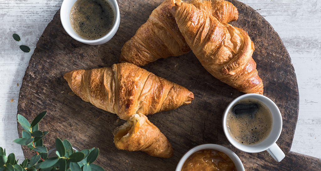 Croissant freschi con caffè espresso su tagliere di legno. Colazione italiana.