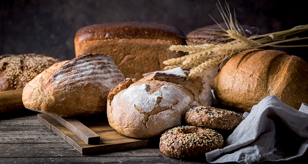 Assortimento di pane artigianale: pagnotte integrali, segale e bagel con sesamo. Panificazione tradizionale italiana.
