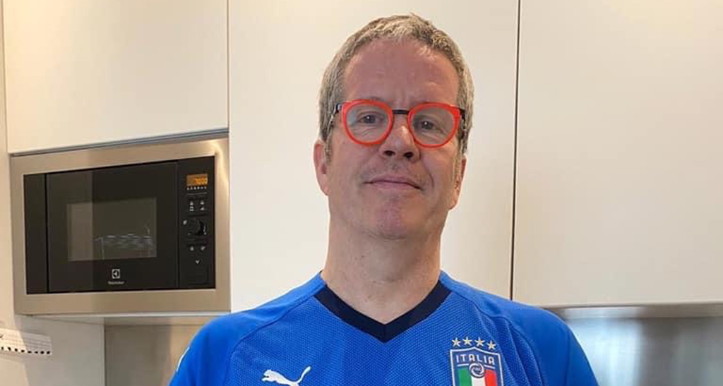 Uomo con maglia Italia, occhiali rossi in cucina. Elettrodomestici moderni.