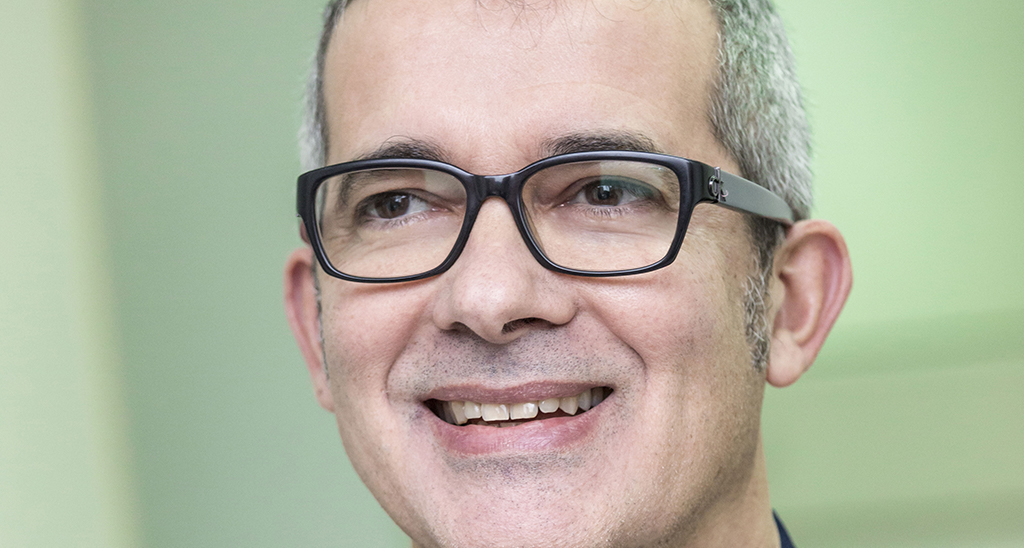 Ritratto del Dr. Motzo con occhiali. Medico sorridente, sguardo professionale.