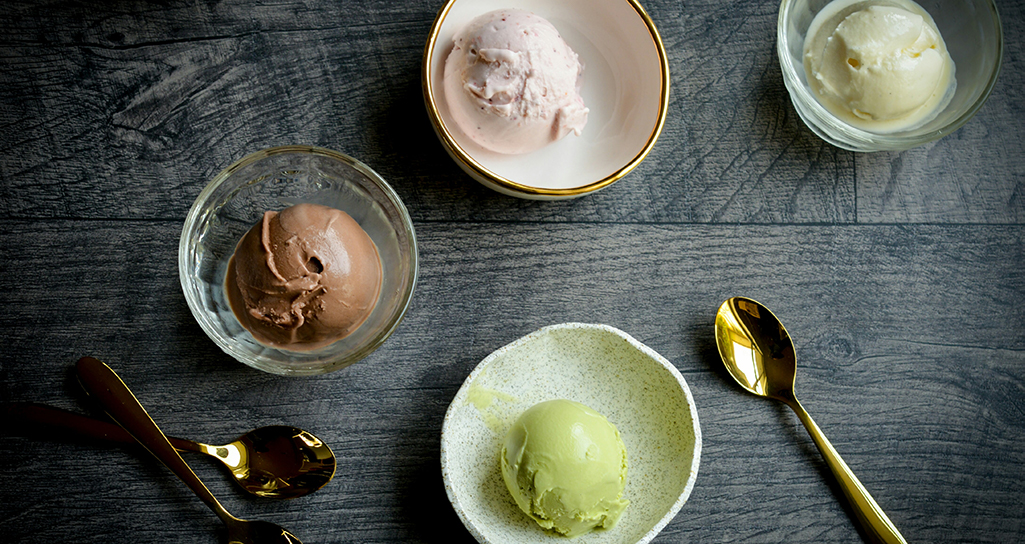 Gelato artigianale: gusti assortiti (cioccolato, fragola, pistacchio, vaniglia) in coppette su tavolo di legno. Cucchiai dorati.