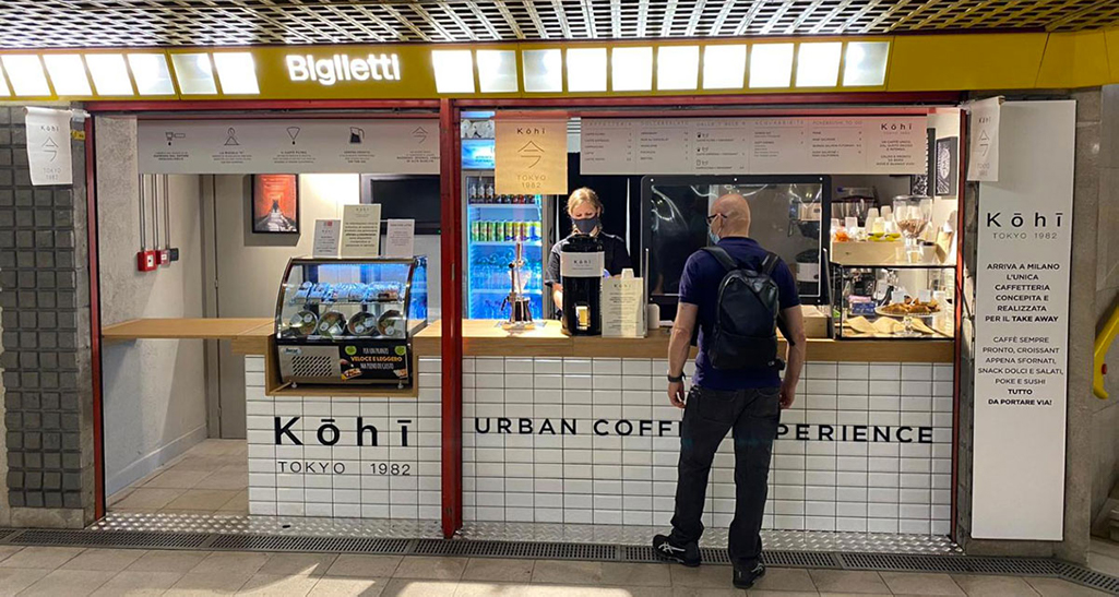Kōhī Tokyo 1982: caffetteria moderna con cliente. Design urbano, caffè da asporto e biglietteria.