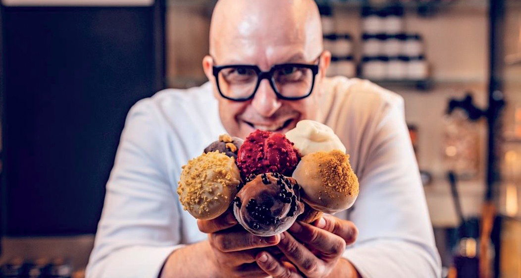 Chef sorridente offre coni gelato artigianale. Gelato gourmet con gusti assortiti e decorazioni uniche.