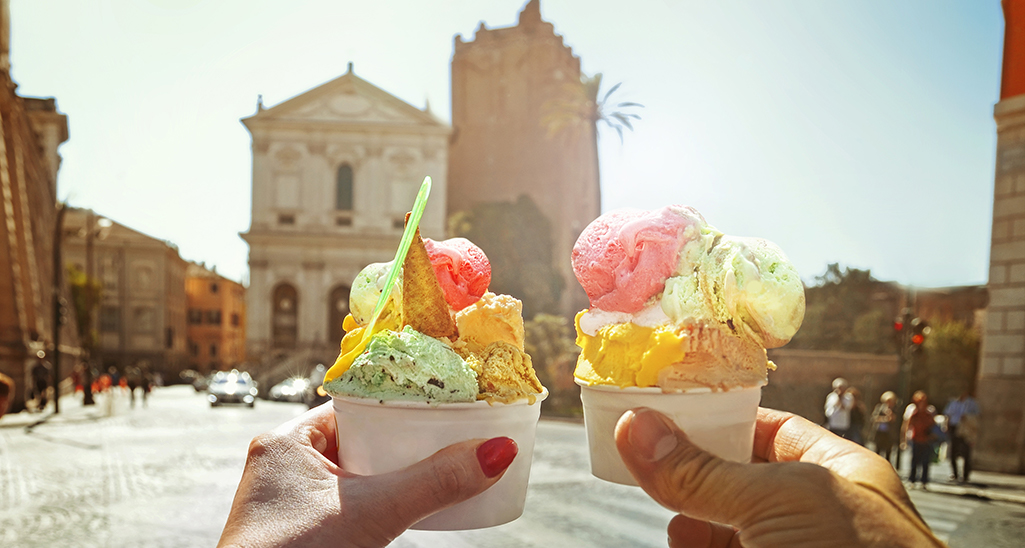 Gelato artigianale italiano a Roma. Mani tengono gelati colorati con sfondo monumenti.