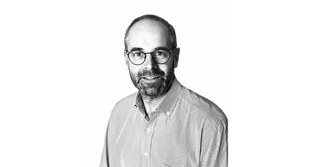 Ritratto in bianco e nero di un direttore commerciale sorridente con occhiali e camicia a righe.