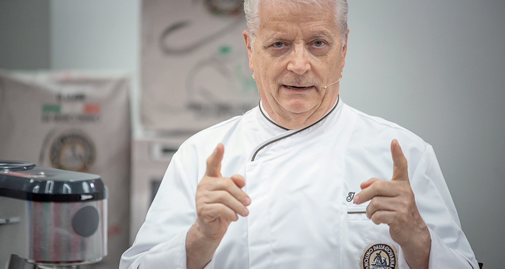 Chef italiano spiega ricetta. Farina, impastatrice e cucina professionale.