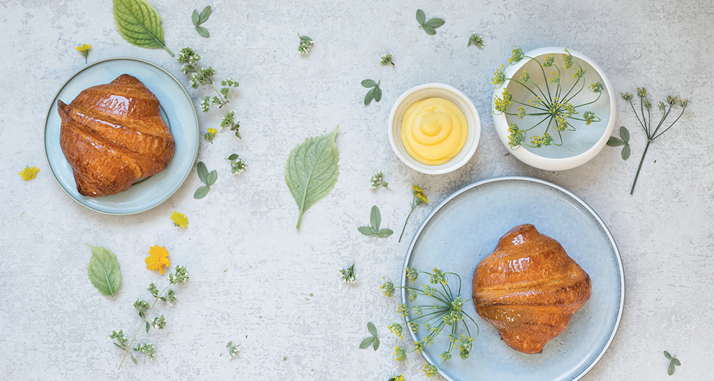 Croissant dorati su piatti, crema, fiori. Colazione dolce e primaverile.