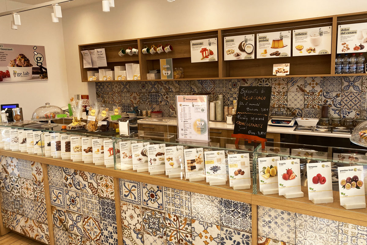 Gelateria artigianale: banco con mosaico, gusti gelato esposti. Menù e decorazioni in legno.