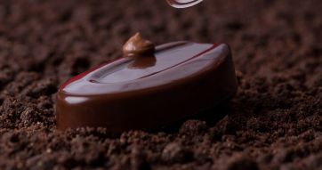 Cioccolatino Valrhona lucido su crumble di cacao. Pasticceria artigianale, dessert gourmet.
