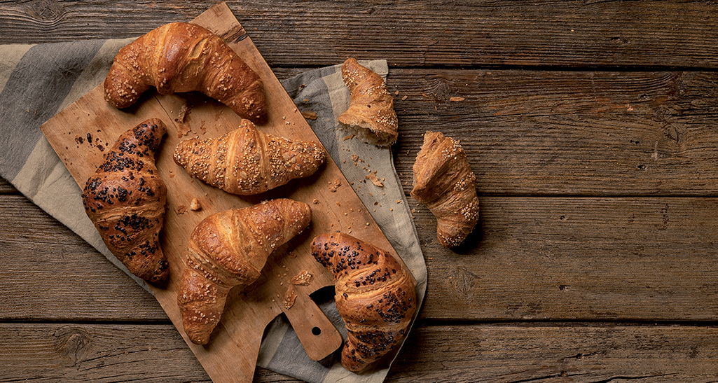 Croissant freschi su tagliere di legno. Colazione con croissant al cioccolato e semi di sesamo.