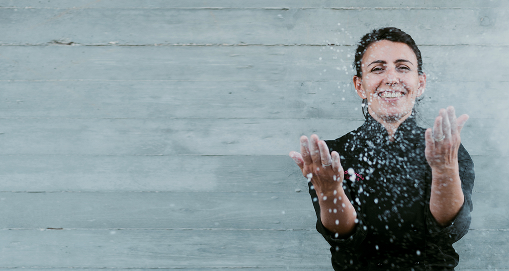 Chef sorridente lancia farina. Cucina, food blogger, donna in divisa nera.