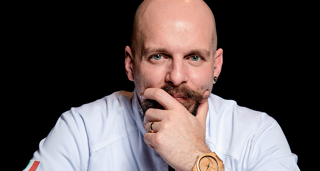 Ritratto dello chef Bertuzzi di Vandemoortele. Primo piano, uomo calvo con barba e orologio di legno.