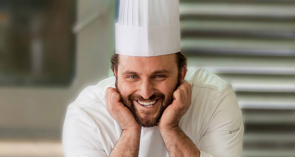 Ritratto dello chef Pietro Macellaro con cappello da cuoco. Sorriso e mani al viso.