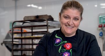 Chef sorridente Stella Ricci. Divisa da cuoco con ricami floreali. Cucina professionale, pasticceria artigianale.