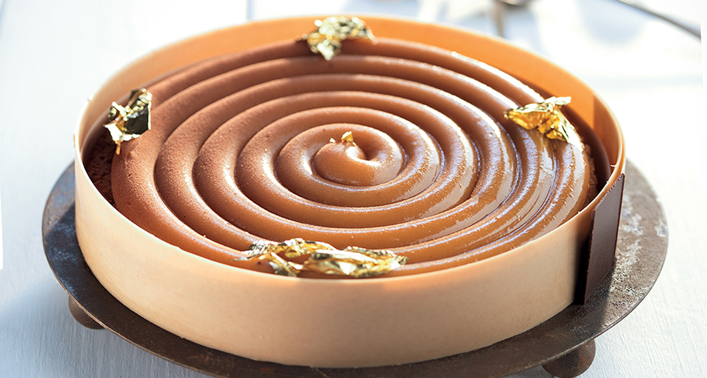 Elegante torta al cioccolato con spirale di caramello e decorazioni in foglia d'oro. Pasticceria raffinata.