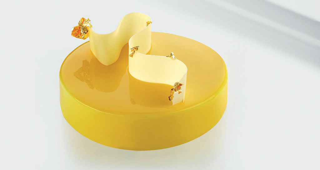 Torta Fusto Milano Luce: dessert giallo lucido con decorazioni dorate e spirale di cioccolato bianco. Pasticceria artigianale.
