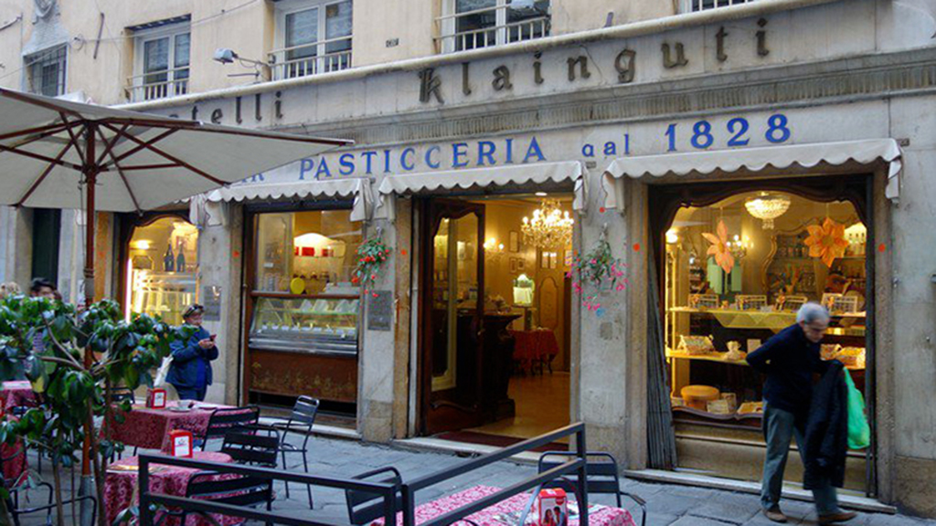 Esterno della Pasticceria Klainguti, Genova dal 1828. Tavolini all'aperto e vetrine illuminate.