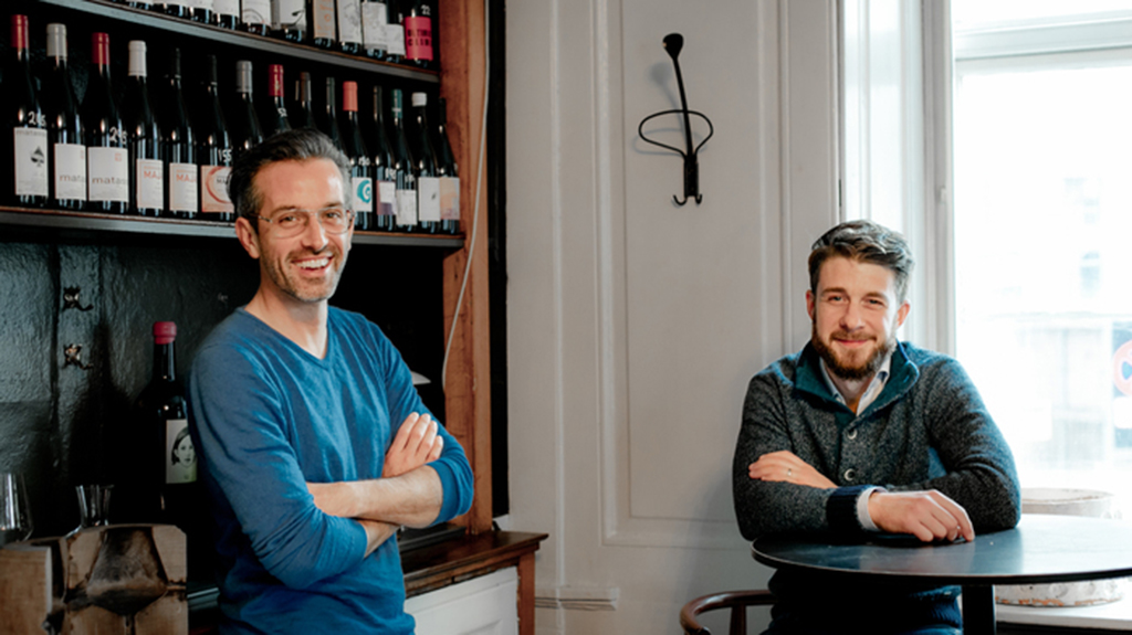 Due uomini sorridenti in un caffè con scaffale di vini. Atmosfera accogliente, locale.