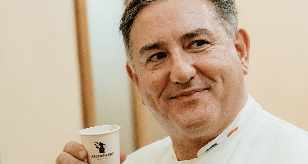 Sal De Riso con caffè Hausbrandt. Chef sorridente in divisa bianca. Eccellenza pasticcera italiana.