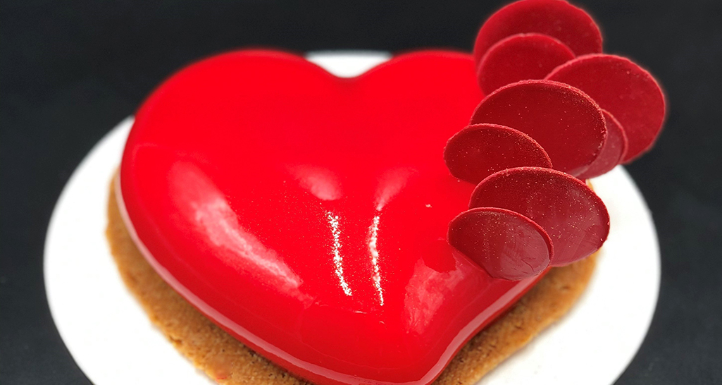 Torta a forma di cuore rosso lucido con decorazioni. Dolce romantico per San Valentino.