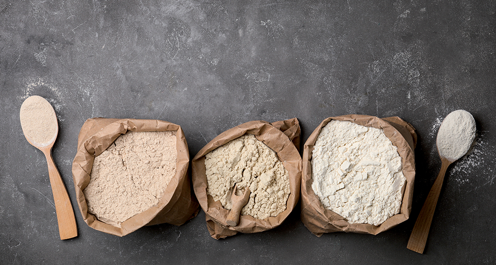 Assortimento di farine bio in sacchi di carta. Farina integrale, farina di grano tenero, cucchiai di legno.