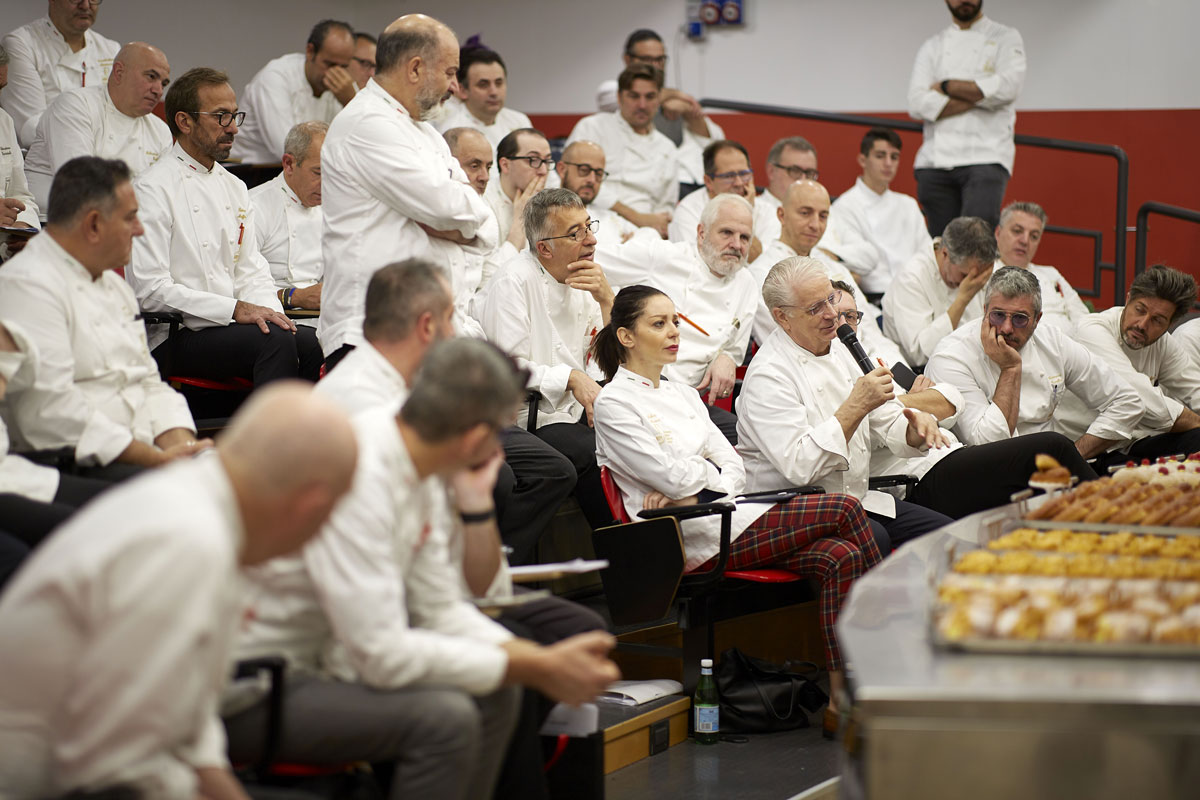 Direttivo AMPI: pasticceri riuniti in assemblea. Chef in divisa bianca ascoltano un oratore. Colazione dolce.