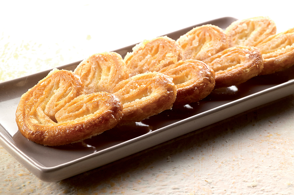 Dolci palmiers su piatto. Biscotti sfoglia a forma di cuore, croccanti e dorati. Perfetti per colazione o merenda.