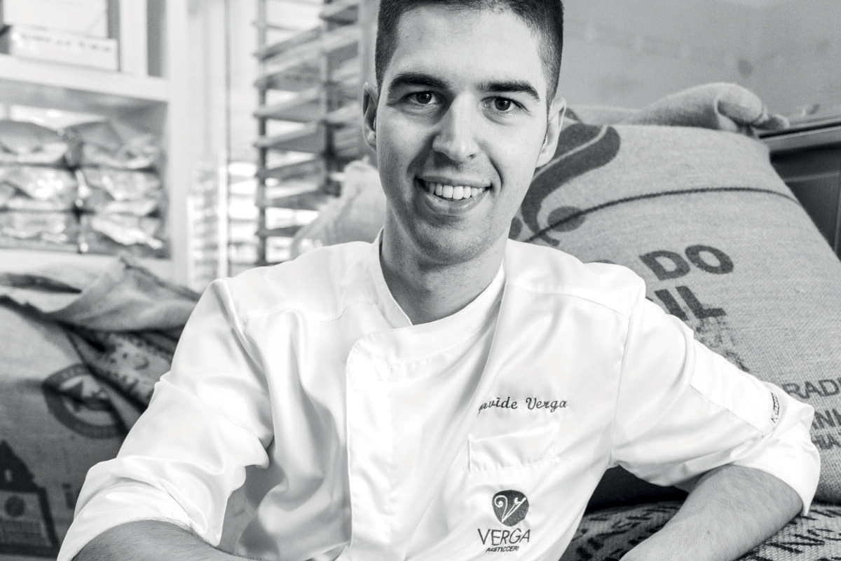 Davide Verga, pasticcere. Ritratto in bianco e nero, sacchi di farina sullo sfondo. Pasticceria Verga.