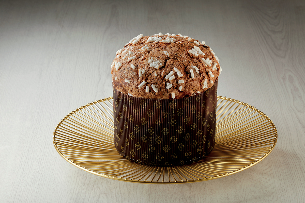 Panettone artigianale al cioccolato con granella, su piatto dorato. Dolce natalizio.