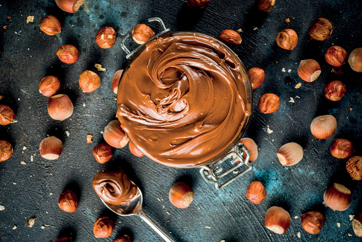 Pasta insaporente: vasetto di crema spalmabile alle nocciole, 100% made in Italy. Cucchiaio e nocciole.