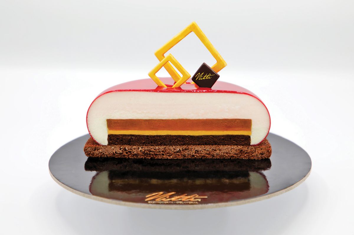 Torta Puglia Nitti: sezione con strati di crema, cioccolato e glassa rossa. Decorazioni geometriche.