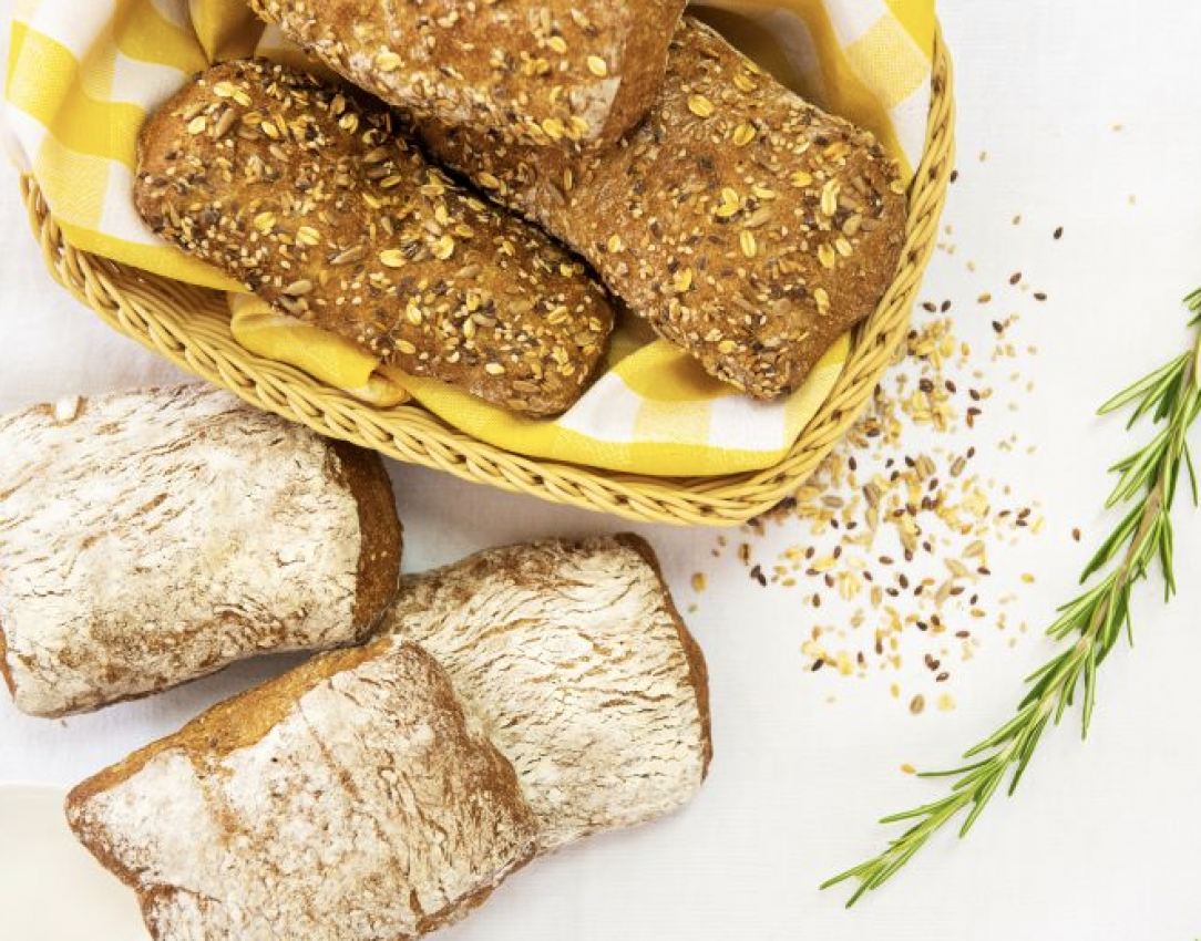 Pane artigianale: ciabatte e panini ai semi in un cesto. Prodotti da forno freschi e gustosi.